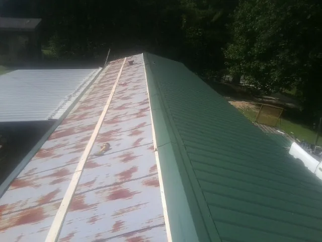 Old rusted panels beside newly installed green metal roofing — Wind Damage Roof Repair by Roofing Brothers in Star